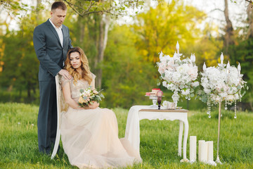 Beautiful young couple in love,bride and groom,the groom-brunette with short hair,the bride a beautiful blonde with long curly hair in white wedding dress sitting at a table outdoors in the Park