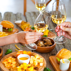 Hands with red wine toasting over served table with food.