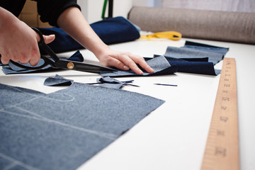 Wall Mural - Hands of seamstress cutting a jeans fabric with scissors on white table