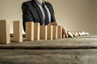 A businessman wearing a suit standing beside a series of vertical wooden slabs as they fall one after another. Concept of domino effect where one business failure causes further collapses.