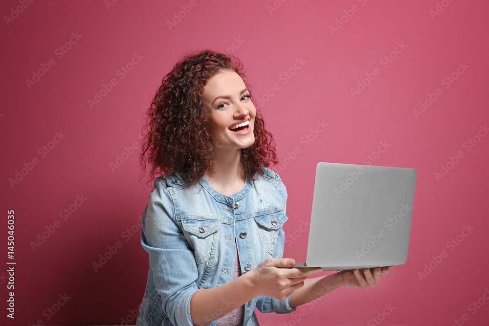 Beautiful young woman using laptop on color background