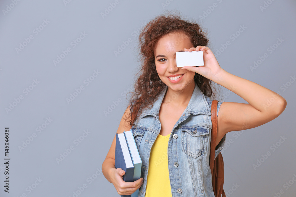 Beautiful African American student with business card on grey background