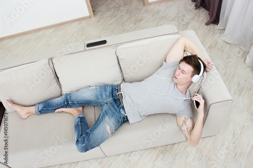 Plakat Mężczyzna słucha muzykę z smartphone w domu na kanapie