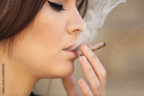 Beautiful young woman smoking weed outdoors, closeup