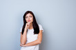 © deagreez - Portrait of young minded woman in white t-shirt touching her chin isolated on gray background