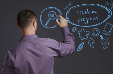 Business, Technology, Internet and network concept. A young businessman writes on the blackboard the word: Work in progress