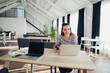 © romankosolapov - Portrait of an attractive woman sitting at the table with a laptop computer holding phone and looking away searching for inspiration for her book.