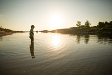 Boy Wading In Water At Sunset
