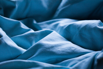 Gently sleeping blue bed sheet in soft morning or evening romantic sunlight as beautiful textile sleep relaxation decorative background