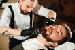 © nagaets - Master cuts hair and beard of men in the barbershop