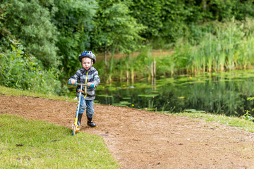 Day view child boy riding scooter summer park