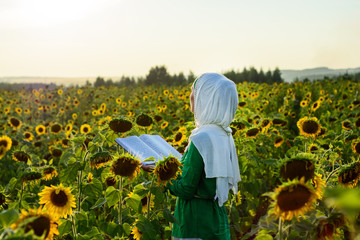 Girl in field of sunflowers, thinking about the Koran.