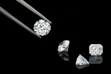 Loose Brilliant Diamonds, Round, Trillion, And Radiant / Emerald On Reflective Black Background One Is Being Held By Tweezers