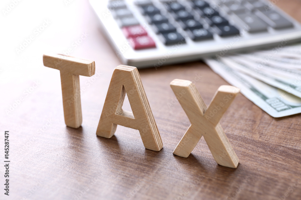 Wooden word "TAX" and calculator on background