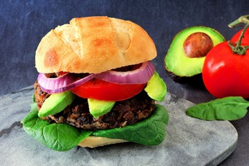 Veggie bean and sweet potato burger with avocado and spinach against a dark background