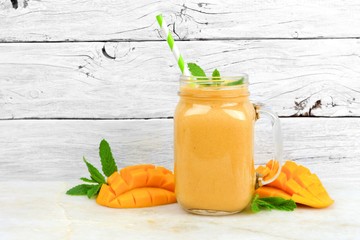 Wall Mural - tropical mango coconut smoothie in a mason jar glass, on a rustic white wood background