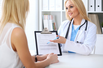 Doctor and  patient  discussing something while physician pointing into medical history form at clipboard. Medicine and health care concept