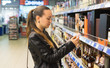 © Igor Kardasov - Woman deciding what wine or alcohol to buy. shopping in supermarket concept