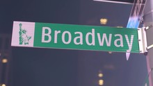 CLOSE UP: Lit Broadway Traffic Sign Mounted On A Pole On A Sidewalk At Iconic Times Square In New York City By Night. Contemporary Glassy Skyscraper And Flashing Ad Billboards In The Background