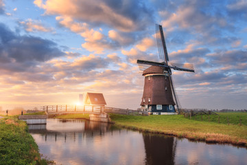 Windmill near the water canal at sunrise in Netherlands. Beautiful old dutch windmill and colorful sky with clouds. Rustic landscape in Holland. Sunny morning. Sky reflected in water. Rural scene