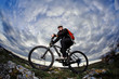 © Aleksey - Cyclist in the black sportwear riding the bike on the rock at evening against beautiful blue sky with clouds.