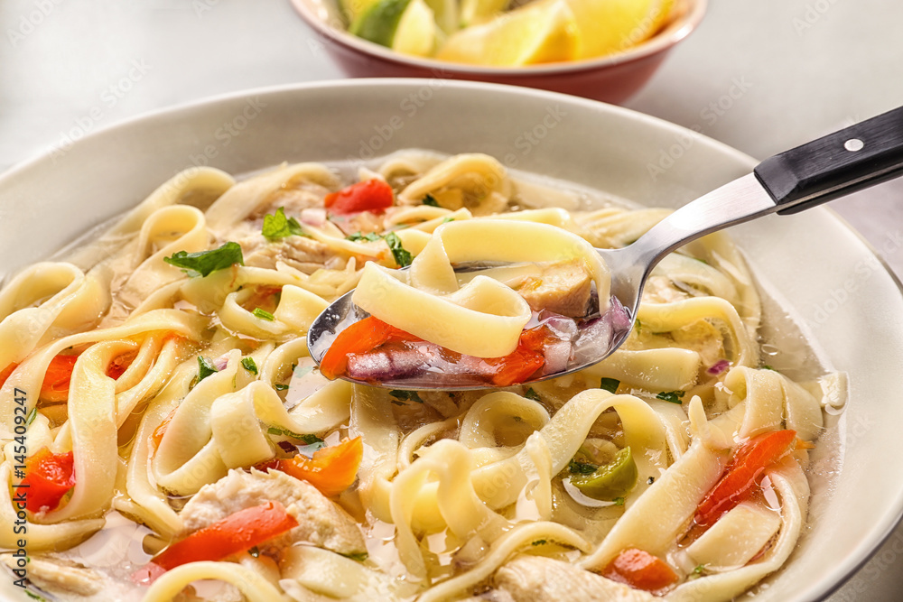 Spoon with chicken noodle soup over plate, closeup