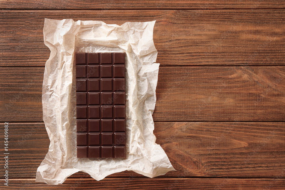 Chocolate bar in parchment on wooden background
