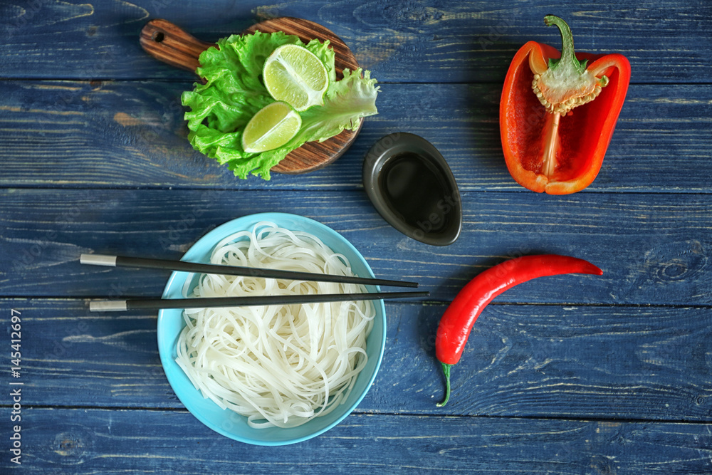 Composition with rice noodles in bowl on wooden table