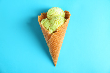 Pistachio ice-cream in waffle cone on color background