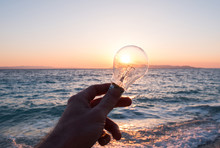 Man Holding Light Bulb Near Sea At Sunset