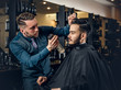 © Fxquadro - Hairdresser doing haircut to a bearded man in a barbershop.