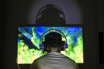 Wall Mural - Young gamer playing video game wearing headphone.