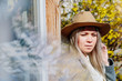 Pensive young blond girl in a hat among the spring flowers closeup. Emotional portrait.