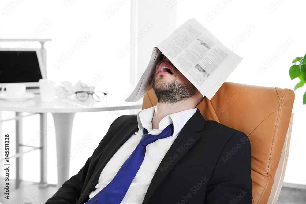 Business man sleeping under newspaper at workplace