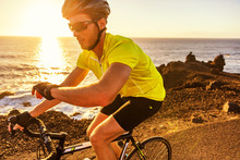 Cyclist Biking Looking At Smartwatch While Riding Road Bike. Athlete Biker Using Activity Tracker Gps Fitness Watch On Biking Workout In Sunset. Sports Man Using His Watch App For Fitness Tracking.