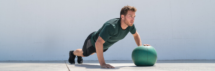 Fitness man banner crop. Athlete strength training pushup chest and shoulder muscles doing alternating single arm medicine ball push-ups floor exercises at outdoor gym.