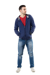 Wall Mural - Cool young guy in blue sweatshirt with hands in pockets looking away. Full body length portrait isolated over white studio background.