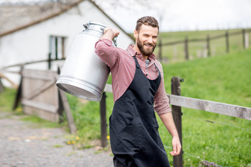 Portrait of a handsome milkman in apron walking with milk container outdoors on the rural scene background