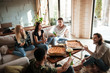 © Drobot Dean - Cheerful young friends eating pizza and talking in living room