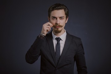 Wall Mural - Studio portrait of a serious young businessman wearing a black suit on black background, copy space