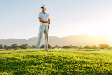 Wall Mural - Male golfer with golf club on field looking away