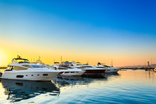 Luxury Yachts Docked In Sea Port At Sunset. Marine Parking Of Modern Motor Boats And Blue Water. Tranquility, Relaxation And Fashionable Vacation.