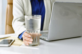 Fototapeta Morze - Business woman drinking fresh water while working at the office, A glass of drinking water on office desk, Drinking for good health concept.