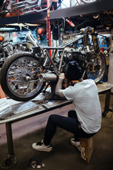 Back view portrait of tattooed man working in garage customizing  motorcycle and repairing broken parts