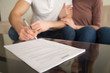 © fizkes - Close up of signing loan agreement, couple sitting on sofa, male hand with a pen setting signature, taking bank credit with easy terms of payment and low interest rate for purchasing property