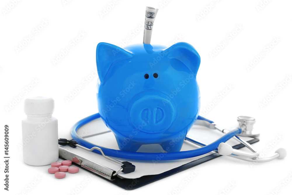 Ceramic piggy bank with stethoscope and pills on white background