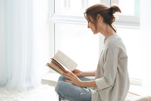 Beautiful Young Woman Reading Book Near Window At Home