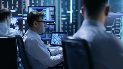 Poster - In the Monitoring Room Team of System Engineers Working at Their Workstations. Multiple Displays Show Various Important Data and Information. Possible Air Traffic/ Power Plant/ Security Room Theme. 