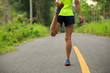 © lzf - Young fitness woman runner stretching legs before running at morning tropical forest trail