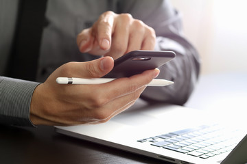 close up of businessman working with mobile phone and stylus pen and laptop computer on wooden desk in modern office